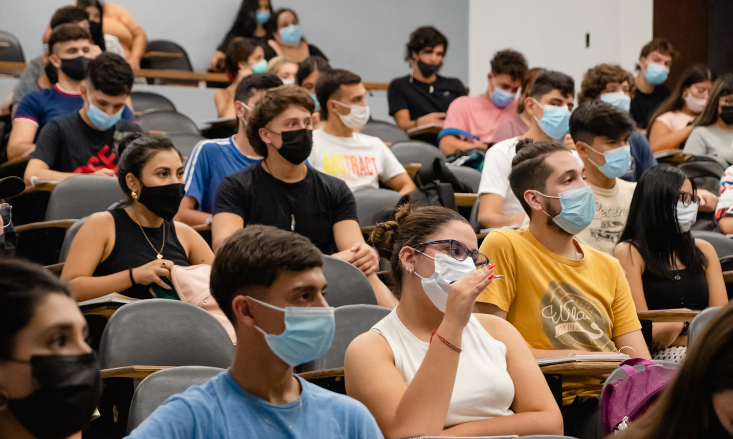 Una treintena de estudiantes varones y mujeres con barbijos sentados en una aula de la Facultad, separados asiento de por medio