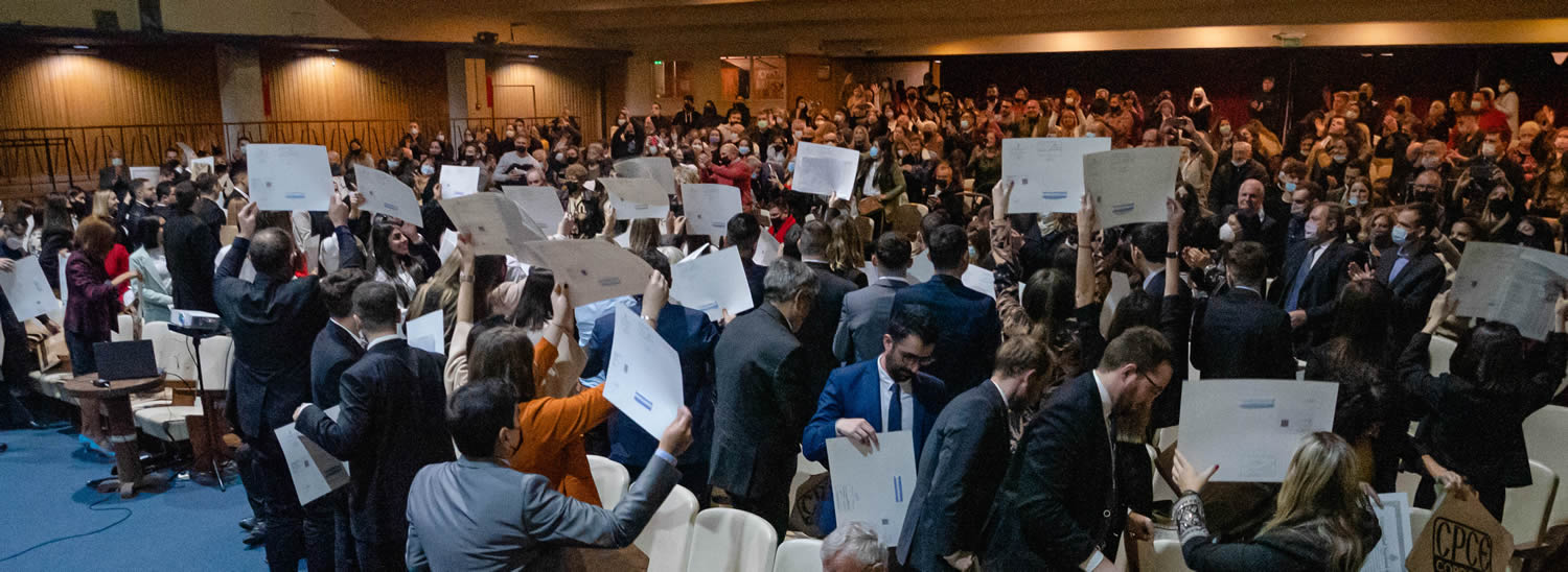 En la Sala de las Américas hay varias luces encendidas contra los muros y un millar de personas de pie aplaudiendo, mientras las personas egresadas muestran sus diplomas elevándolos con sus manos