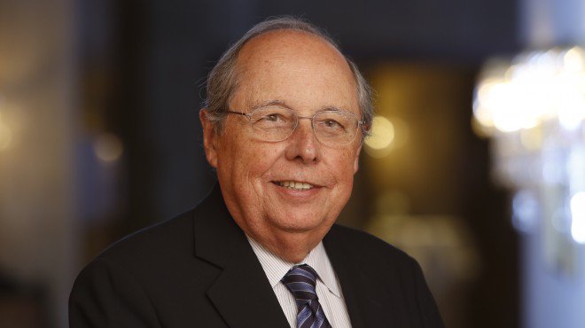 Guillermo Calvo sonriendo, usando lentes y corbata