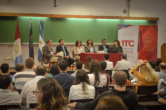 seis personas sentadas en una mesa presentan el evento frente a un auditorio colmado