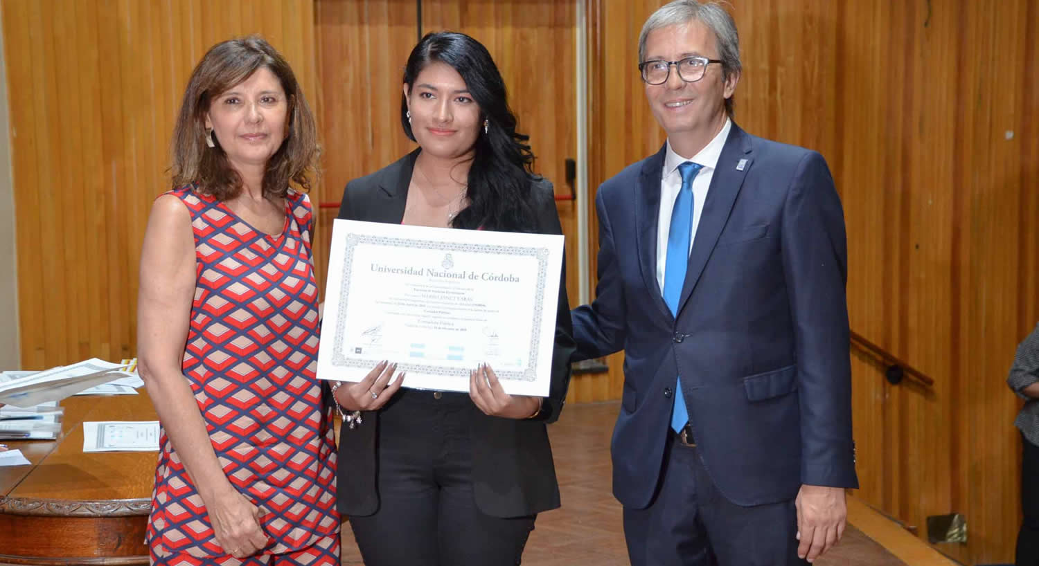 La Vicedecana Catalina Alberto, a la izquierda, y el Decano Jhon Boretto, a la derecha, rodean a una egresada que muestra su diploma