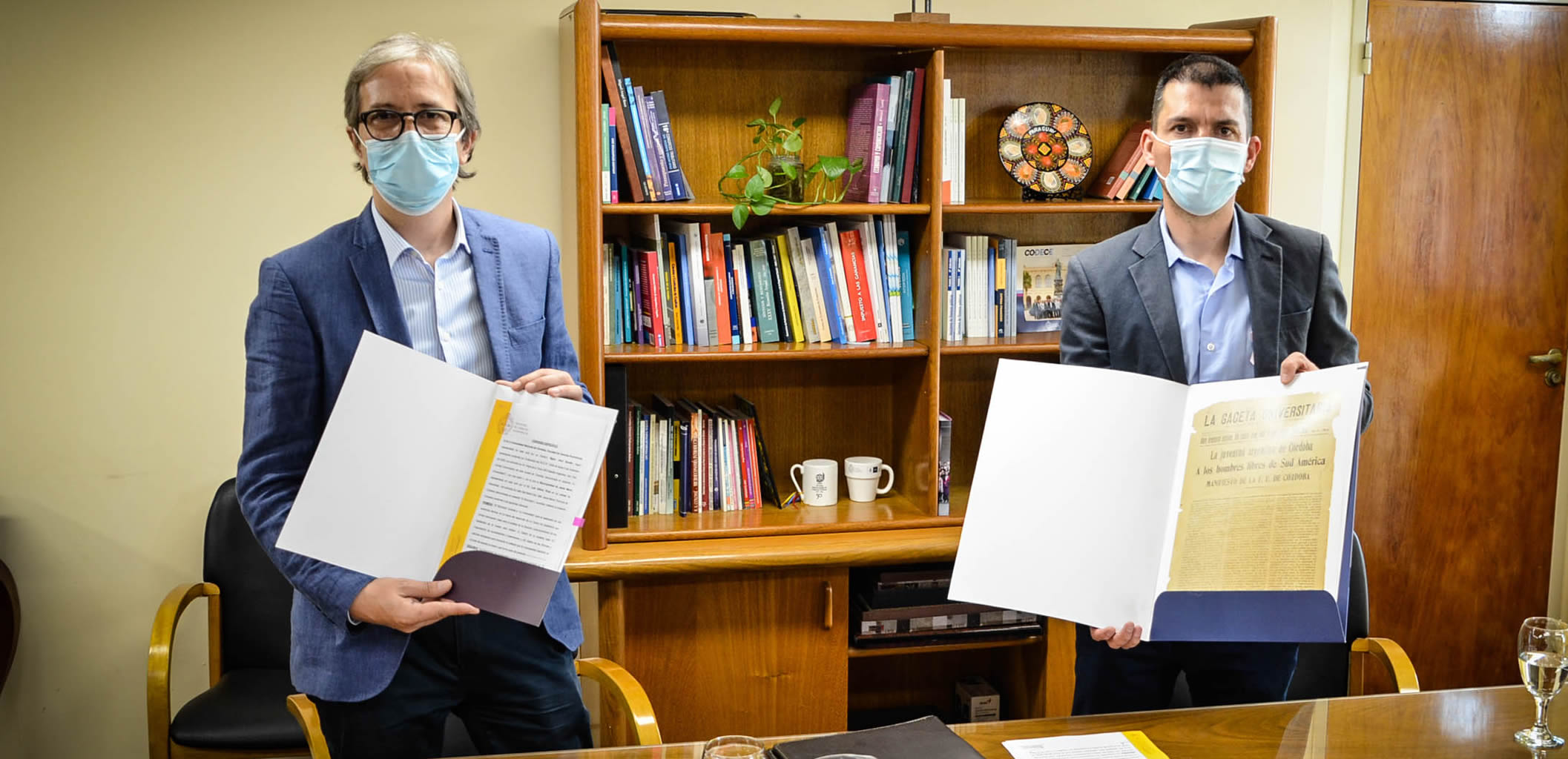 Jhon Boretto y Luis Picat, con barbijos, de pie mostrando el convenio firmado