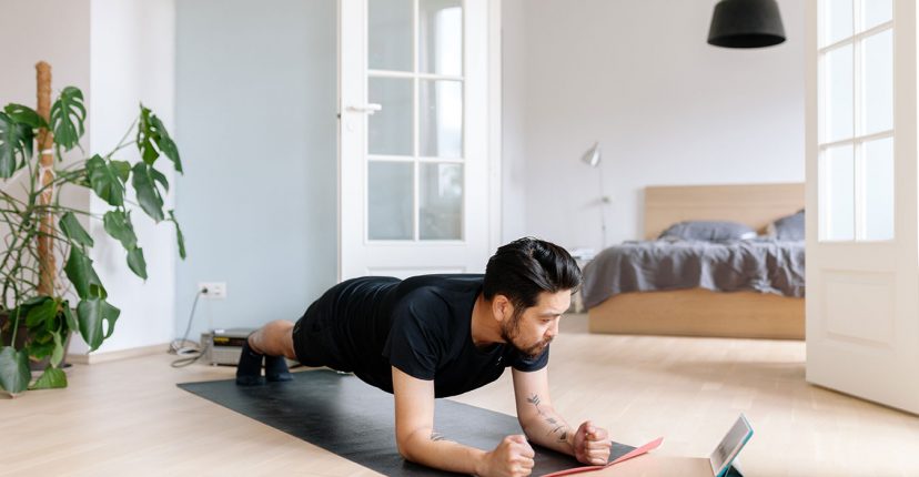 Un varón acostado boca abajo apoyado con sus codos haciendo ejercicios físicos mirando una tablet