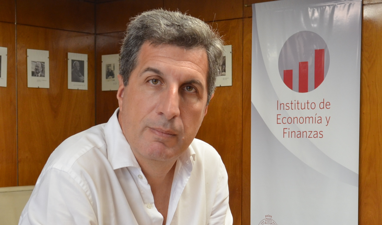 Alejandro Jacobo sentado y detrás el logo del Instituto de Economía y Finanzas