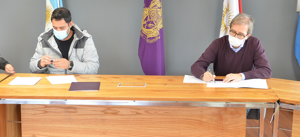 El señor Anconetani y el decano Boretto están sentados y sobre una mesa de madera firman las actas. Detrás están dispuestas en mástiles las banderas de Argentina, la Provincia de Córdoba y la Universidad Nacional de Córdoba.