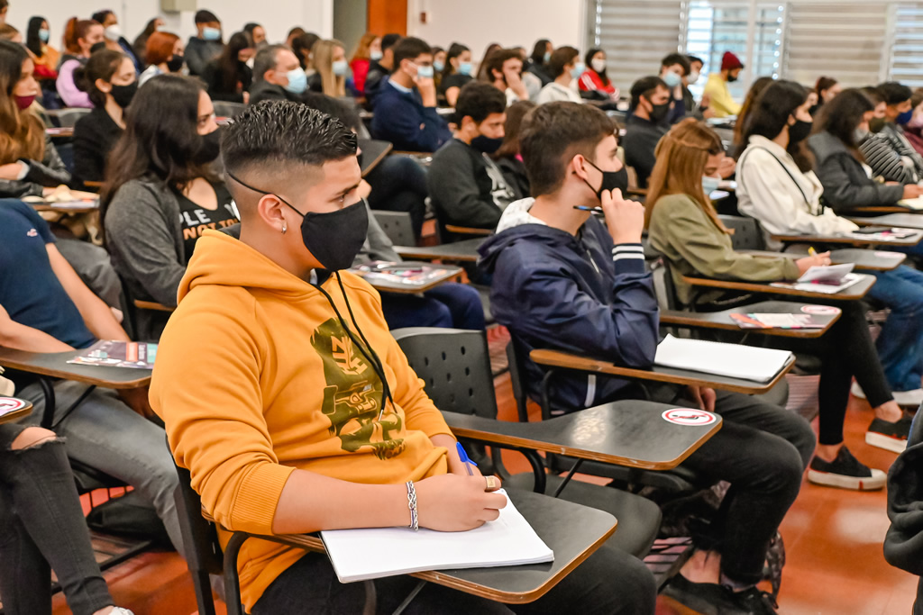 Treinta estudiantes secundarios varones y mujeres sentados en una de las aulas grandes