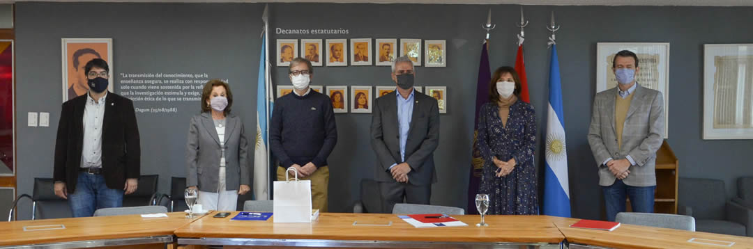 Jhon Boretto, Marcelo Jaluf, Catalina Alberto, María Luisa Recalde, Martín Giorgis y Emiliano Amuchástegui, con barbijos y de pie, con distanciamiento dentro de la sala Camilo Dagum. Detrás están las banderas de Argentina, Córdoba y la Universidad Nacional de Córdoba, y en la pared una serie de cuadros con las fotos de los decanos elegidos democráticamente a lo largo de la historia de la Facultad de Ciencias Económicas