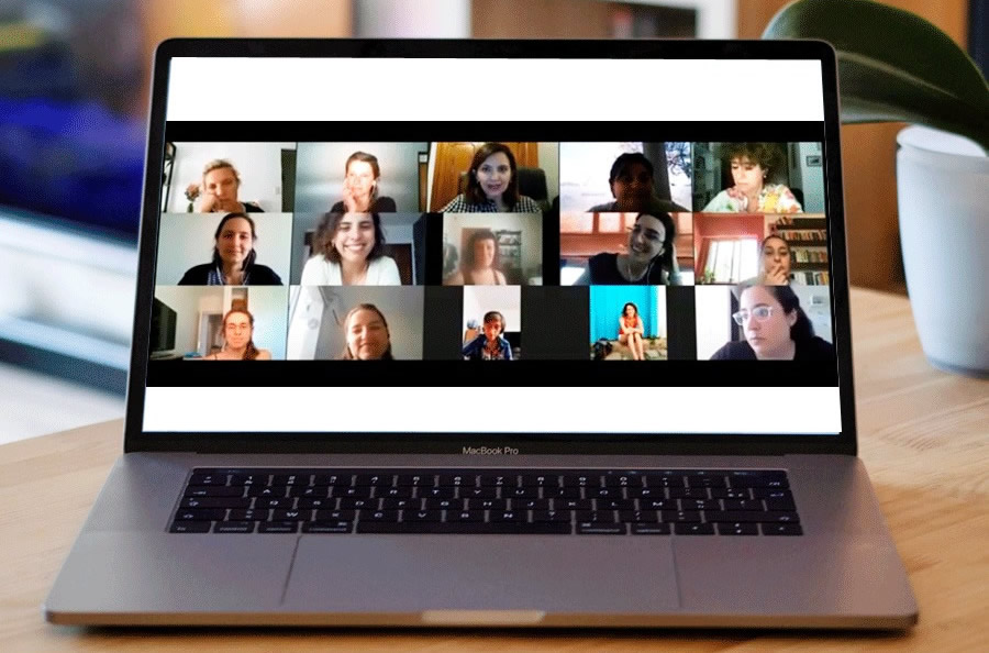 Una computadora portátil sobre una mesa de madera y en la pantalla hay una videoconferencia con varias personas conectadas