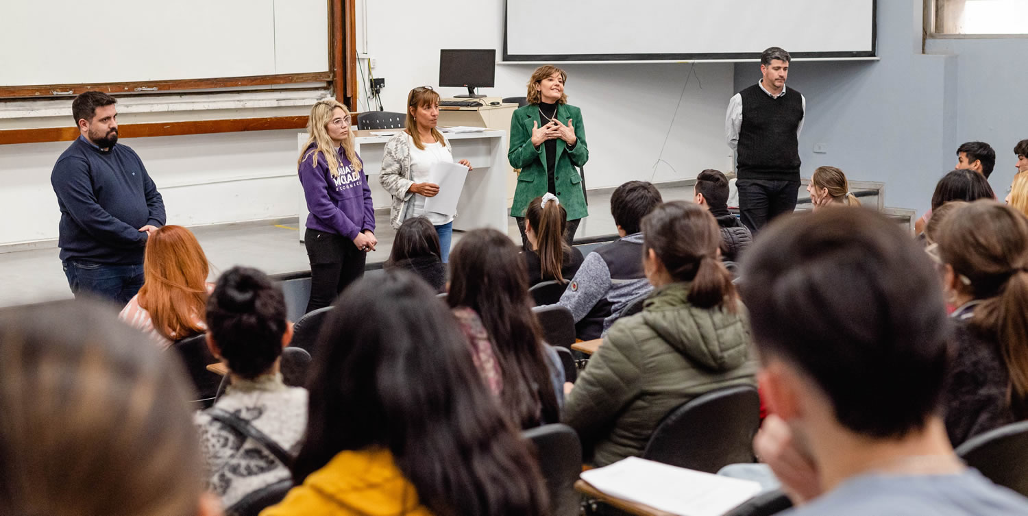 La Decana Catalina Alberto junto a cuatro autoridades más, de pie, frente a una veintena de estudiantes sentados