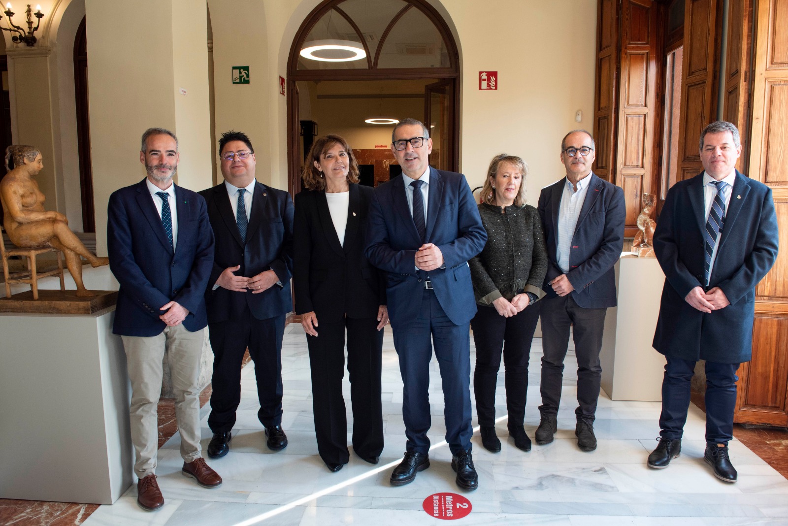 La Decana Catalina Alberto rodeada de cinco funcionarios españoles y el secretario de Asuntos Académicos de nuestra Facultad, de pie sobre un piso de mármol dentro de un amplio recinto iluminado por la luz exterior