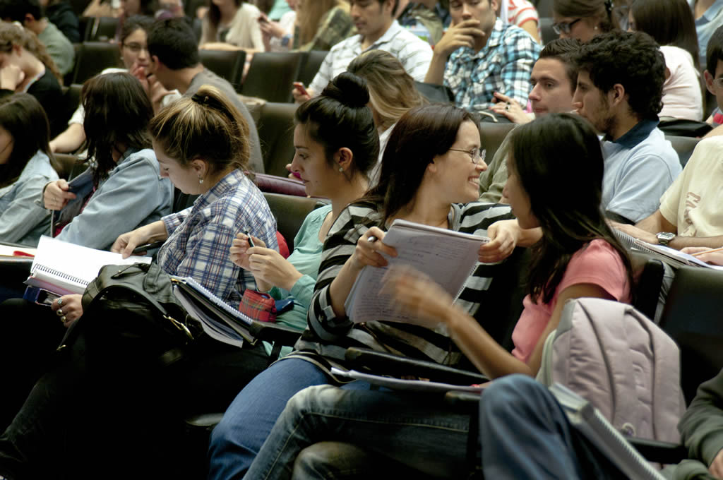 Estudiantes de la Facultad sentados en el aula Magna con cuadernos y leyendo