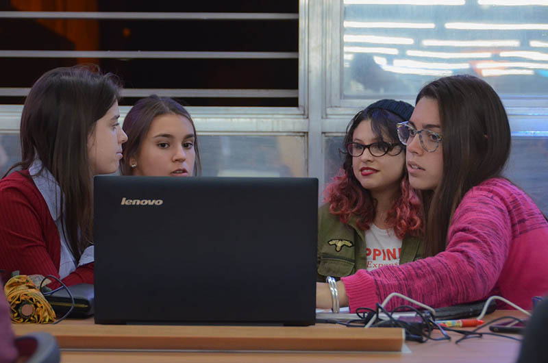 Imagen de cuatro estudiantes mujeres sentadas en una mesa de la biblioteca con una computadora