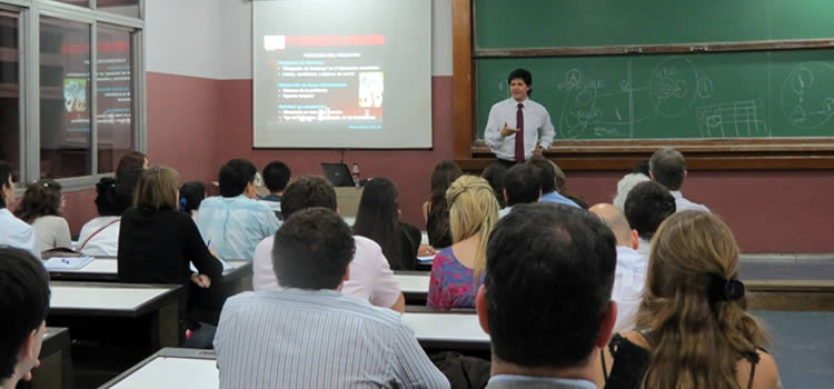 Imagen de un profesor de camisa blanca y corbata roja de pie dando una clase