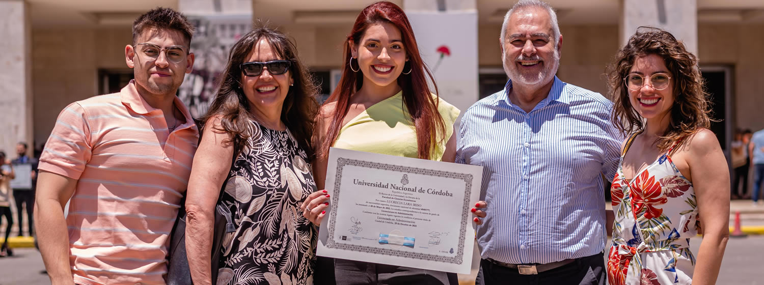 Una egresada muestra su diploma rodeada de dos familiares varones y dos familiares mujeres frente al Pabellón Argentina en un día soleado