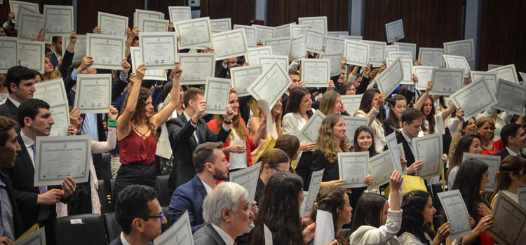 Un centenar de graduados en un acto de Colación de grados de pie y elevando sus diplomas