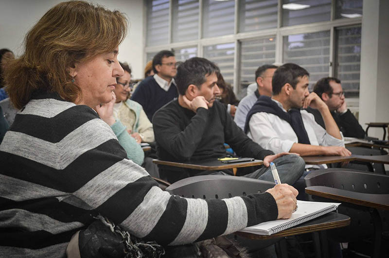 Una profesora escribe en un cuaderno y detrás hay una decena de docentes sentados