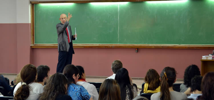 Un docente señala mientras habla a un auditorio con una veintena de alumnos