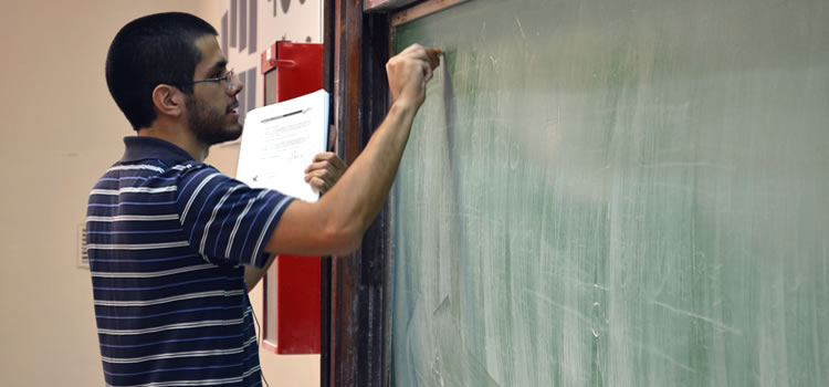 Un joven docente escribiendo con tiza sobre una pizarra