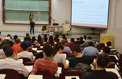 Una docente en un aula explicando una filmina frente a una treintena de estudiantes