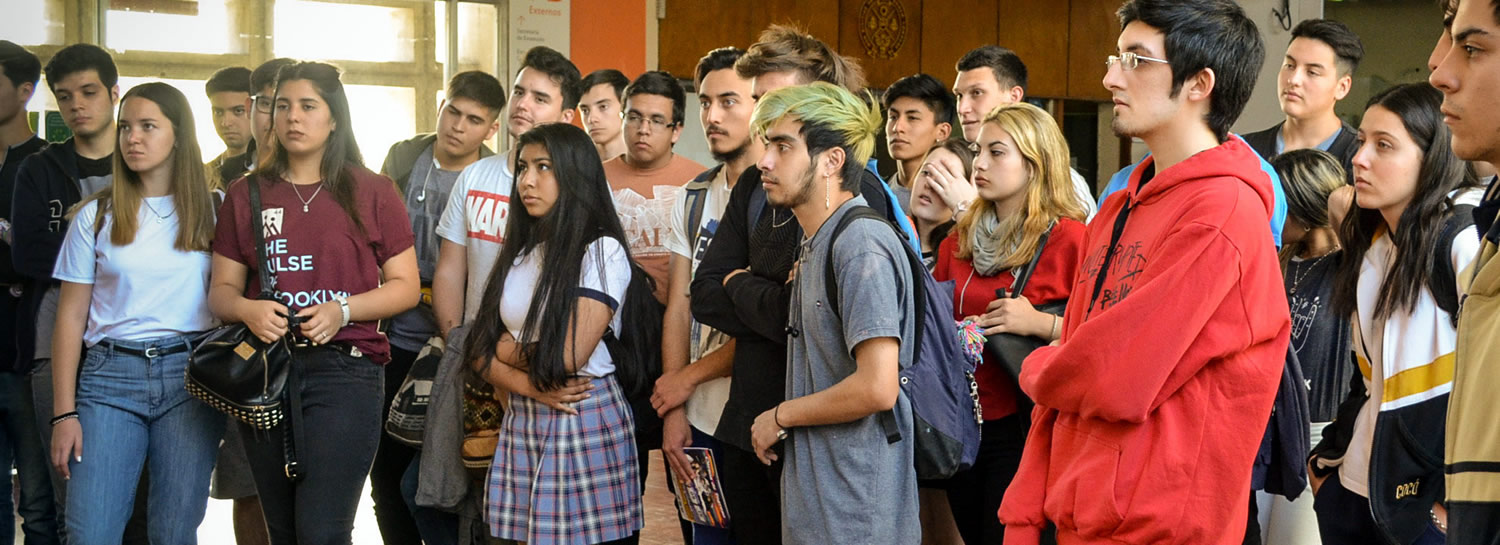Una treintena de estudiantes de escuelas secundarias, de pie, escuchando atentamente dentro del hall central de la Facultad lo que dice la guía de un Eco Tour, en un día soleado