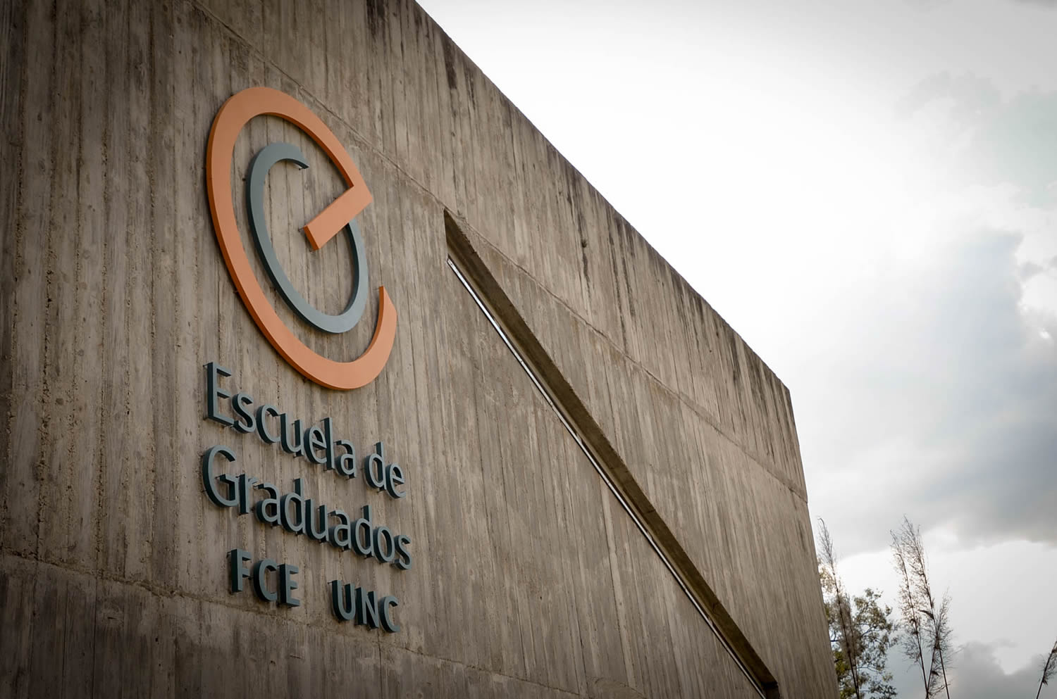 Una pared lateral del edificio de la Escuela de Graduados donde está instalado el logotipo de la Escuela. El día está nublado