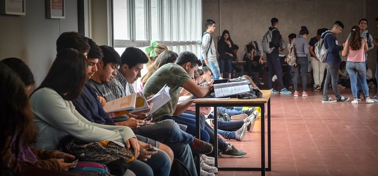 Imagen de estudiantes sentados y de pie en el espacio de acceso al aula O de la planta baja del edificio