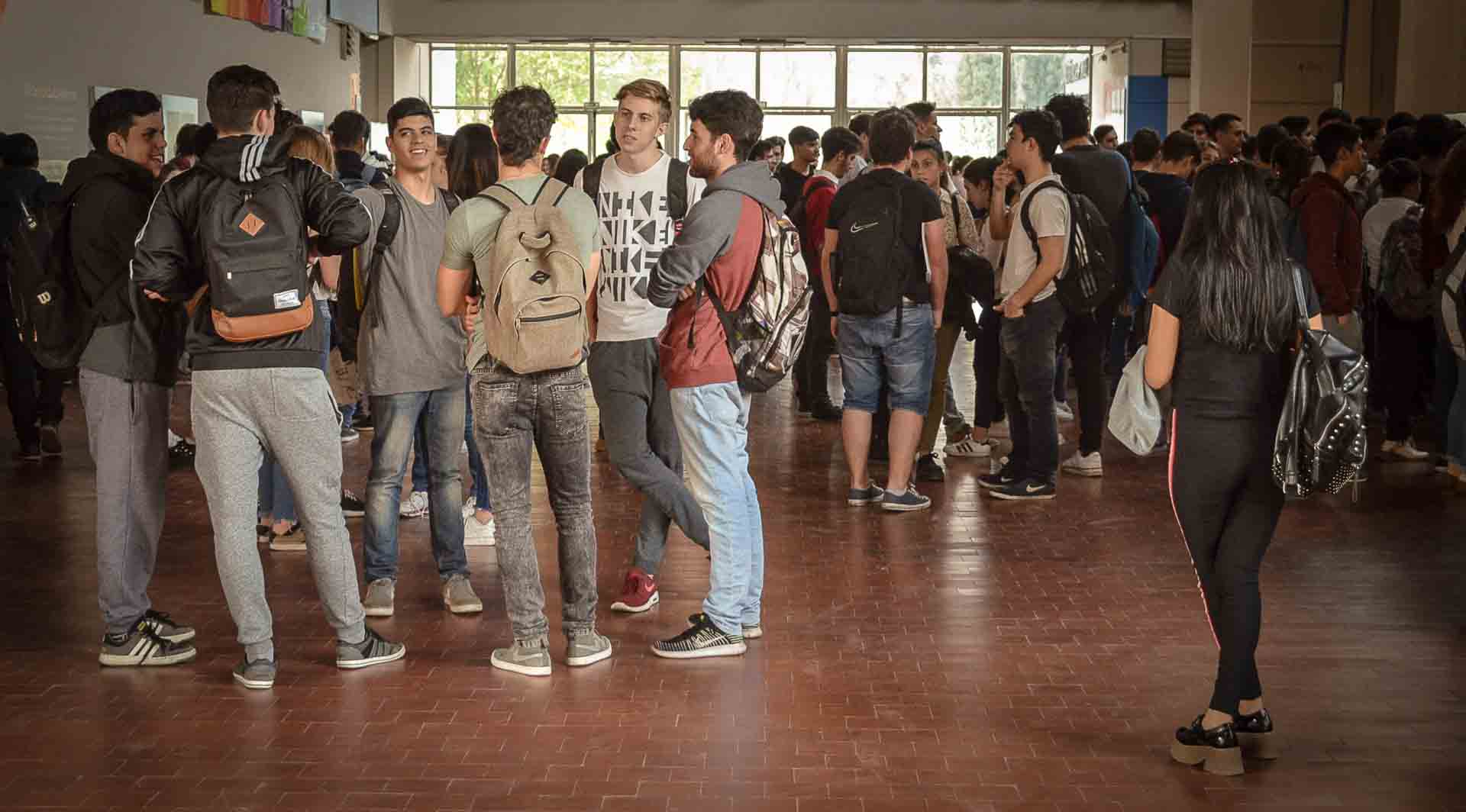 20 estudiantes de pie en el hall central de la Facultad conversando