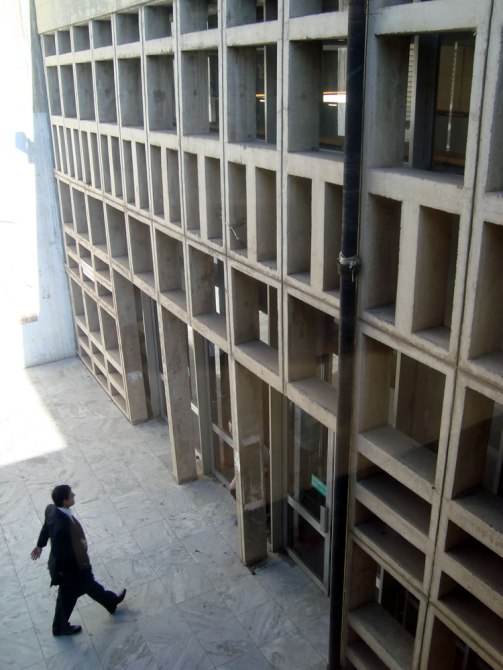 Uno de los costados del edificio de la Facultad donde una mujer está caminando para entrar por la puerta