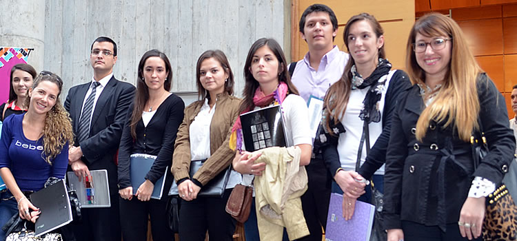 Siete mujeres y dos varones estudiantes de la Escuela de Graduados, de pie, portando carpetas, abrigos y bolsos en sus manos