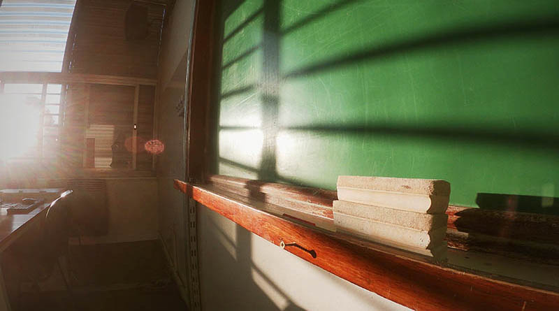Un pizarrón limpio sin escrituras en un aula y hay cuatro borradores de madera, en un atardecer en el que el sol brilla sobre ese espacio