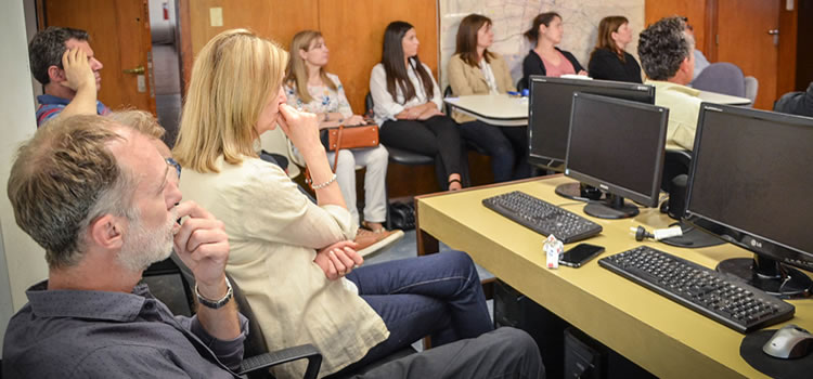 Una docena de profesores y profesoras sentados y hay tres computadoras en una mesa