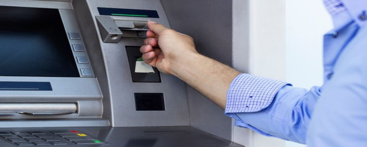 Un varón con camisa arremangada inserta una tarjeta de débito en un cajero automático