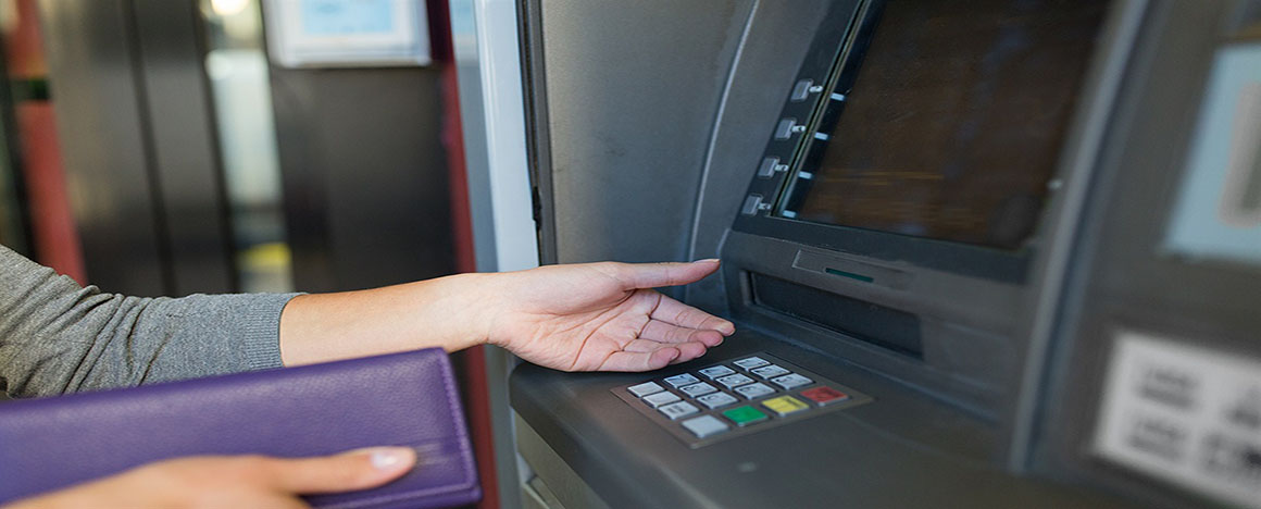 Una mujer con un sobre en una mano y la otra mano está por recibir dinero de un cajero automático