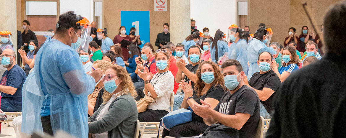 Un centenar de personas sentadas con barbijos dentro del Pabellón Argentina y un enfermero con máscara prepara una vacuna