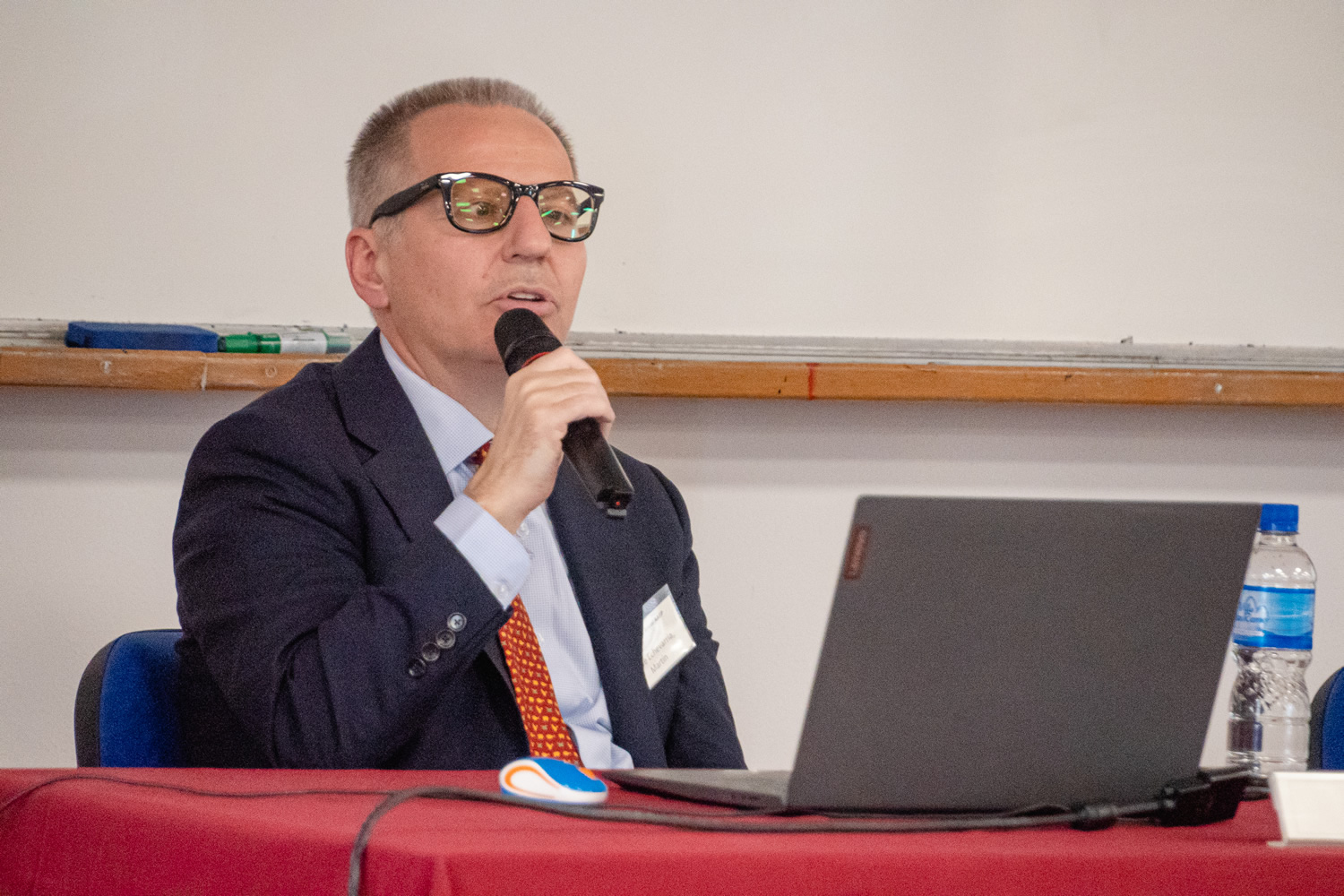 Martín Uribe usando lentes exponiendo usando un micrófono