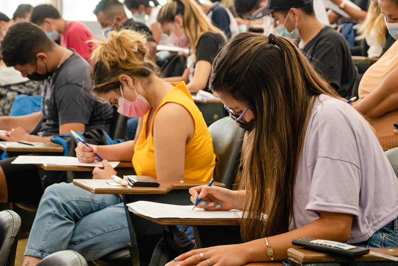 Una docena de estudiantes sentados usando barbijos y escribiendo