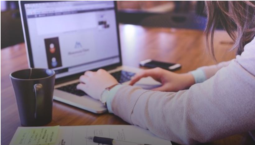 Una persona con sus manos sobre una computadora portátil sobre una mesa con una taza y papeles